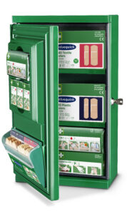 A green first aid cabinet with an open door displaying various first aid supplies, including textile and plastic bandages, a protection kit, and quick bandage dispensers. Instructional diagrams for using the supplies are visible on the inner panel of the door.