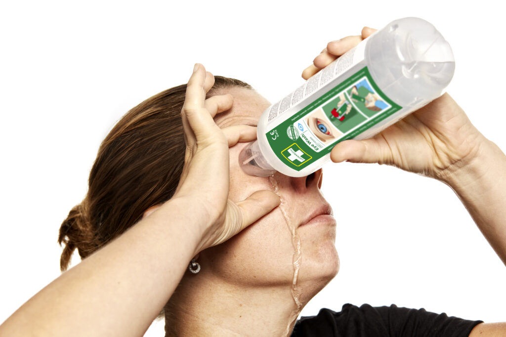 Une personne verse un liquide d'une bouteille transparente sur son visage, les instructions visibles sur l'étiquette verte.